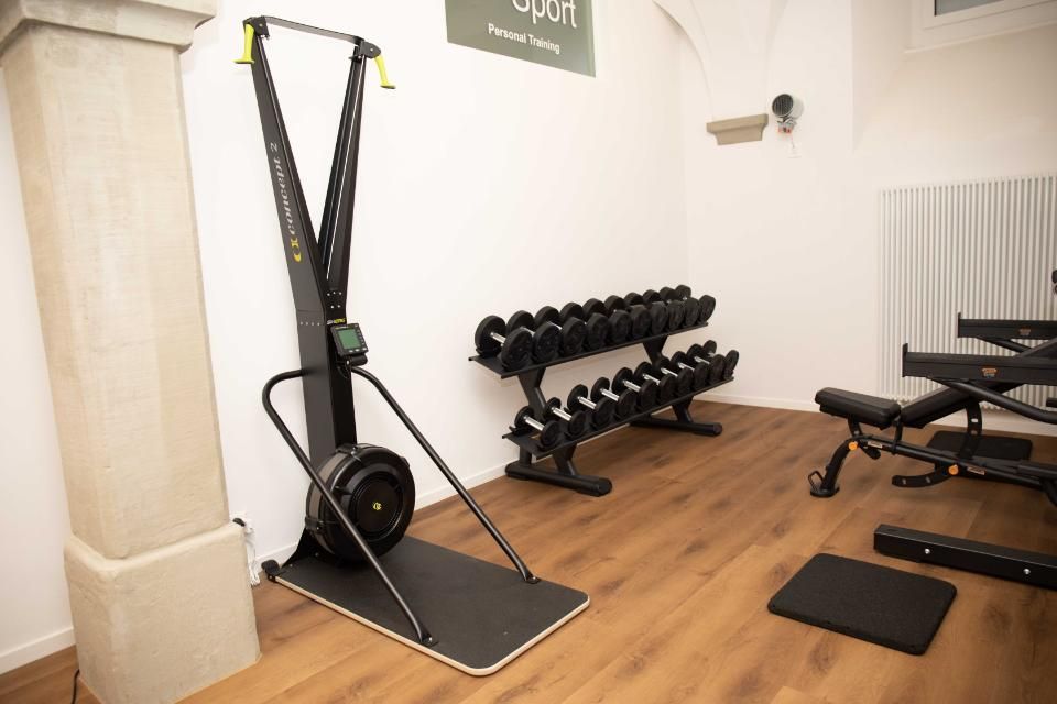 Fitnessstudio-Interieur mit Ski-Ergometer, Hanteln und verstellbarer Bank.