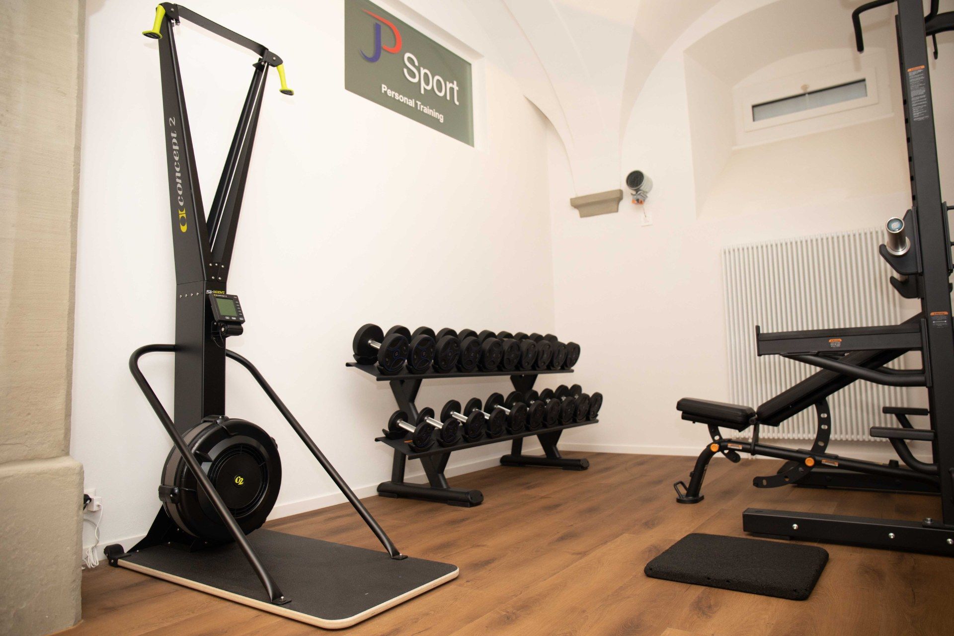 Fitnessstudio-Interieur mit Fitnessgeräten: Skimaschine, Hanteln, Bank und Gewichtsständer.