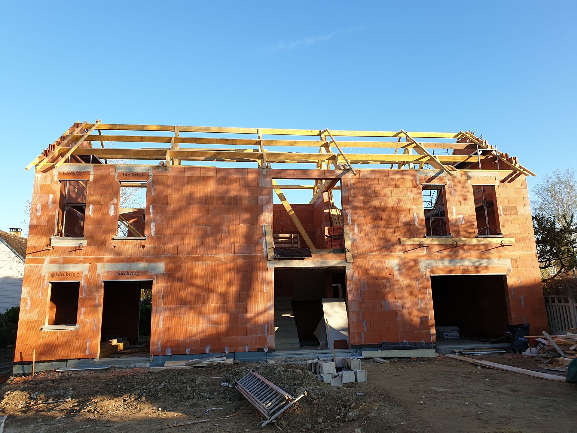 Une maison en briques rouges de deux étages en construction, avec une charpente apparente en bois.