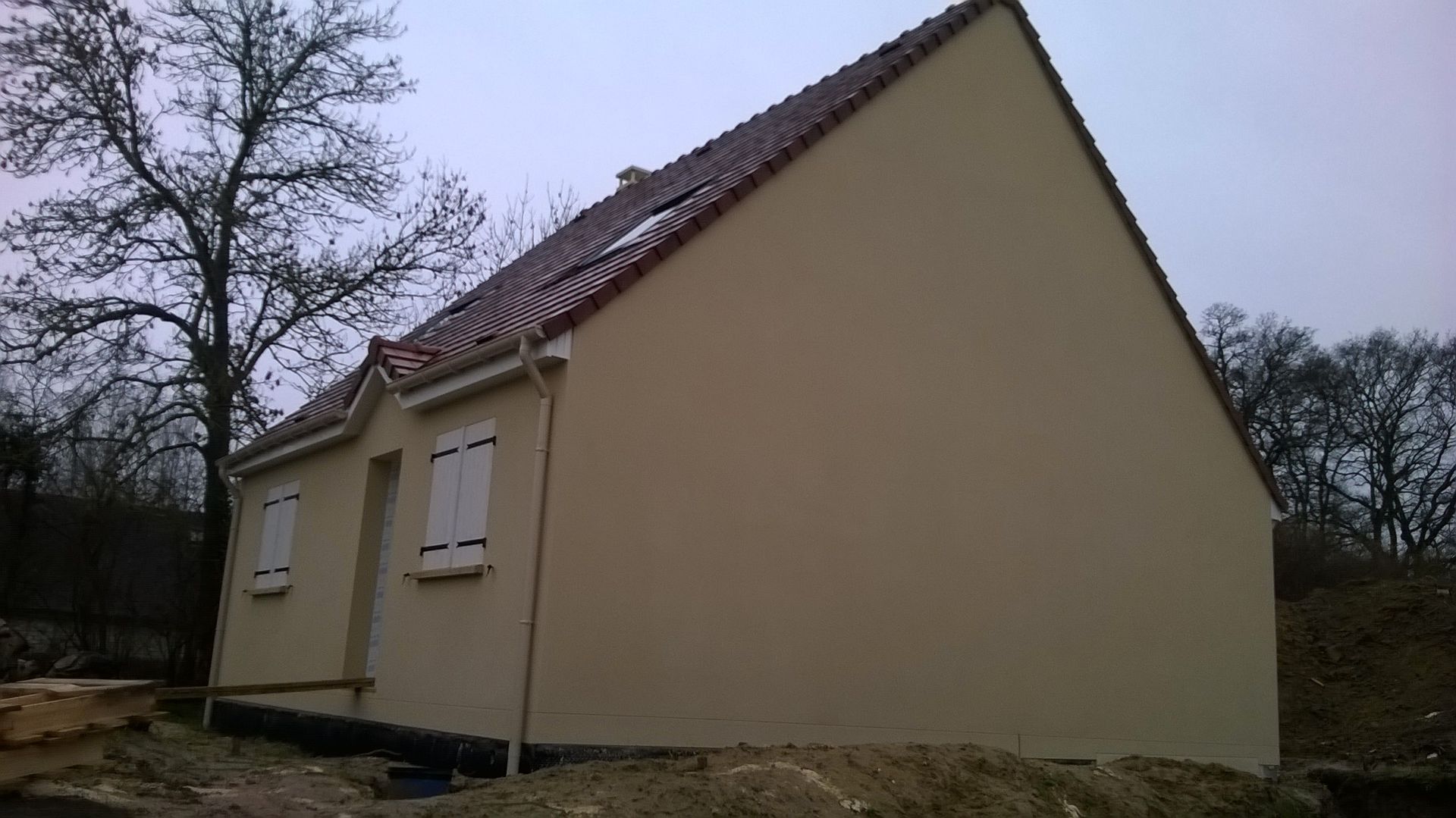 Une maison beige aux volets blancs et au toit de tuiles foncées.