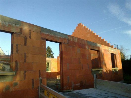 La structure d'une maison en construction, avec des murs de briques orange et des ouvertures pour les fenêtres et les portes.