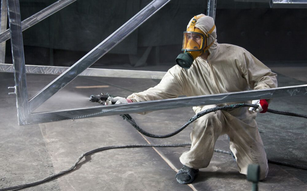 Personne en combinaison de protection pulvérisant une structure métallique dans un atelier.