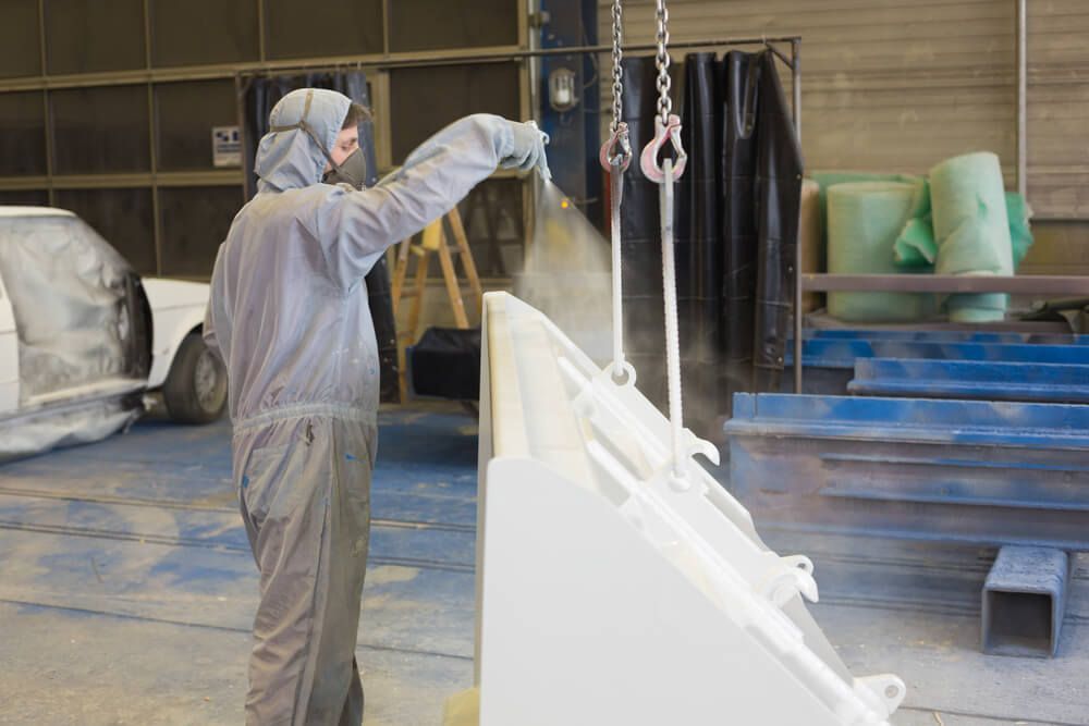 Un ouvrier en combinaison de protection pulvérise de la peinture sur des équipements métalliques dans un atelier.