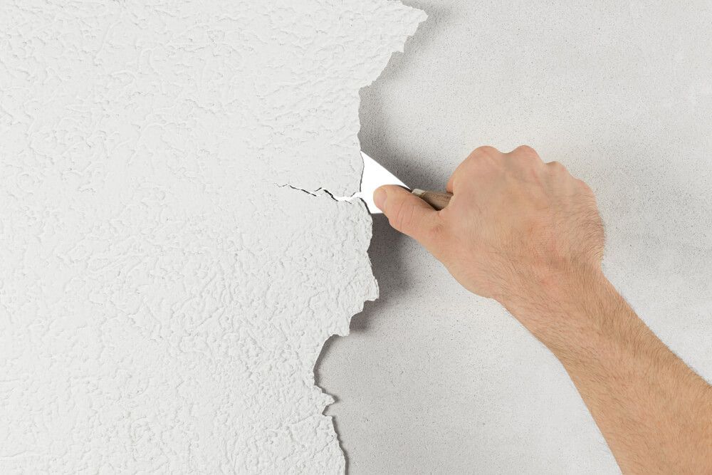 Décoller à la main de la peinture blanche écaillée d'un mur à l'aide d'un couteau à mastic.