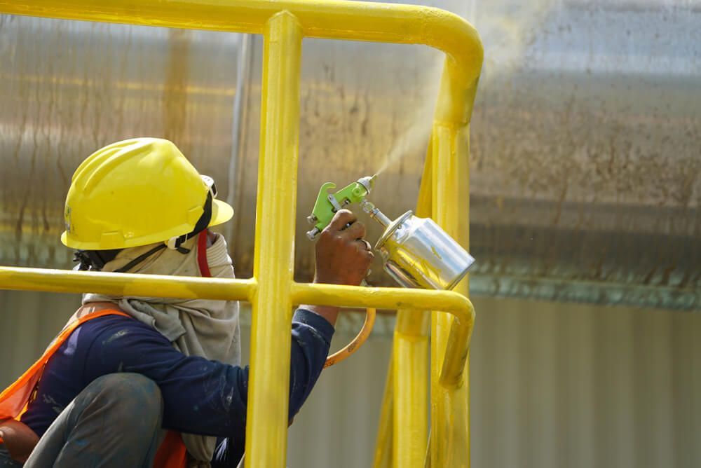 Une personne portant un casque de chantier jaune peint à la bombe en jaune une rambarde métallique à l'extérieur.