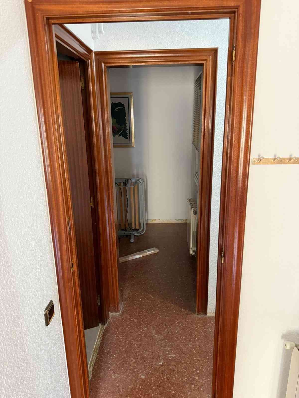 Marcos de madera en las puertas que dan a un pasillo con paredes blancas y suelo marrón.