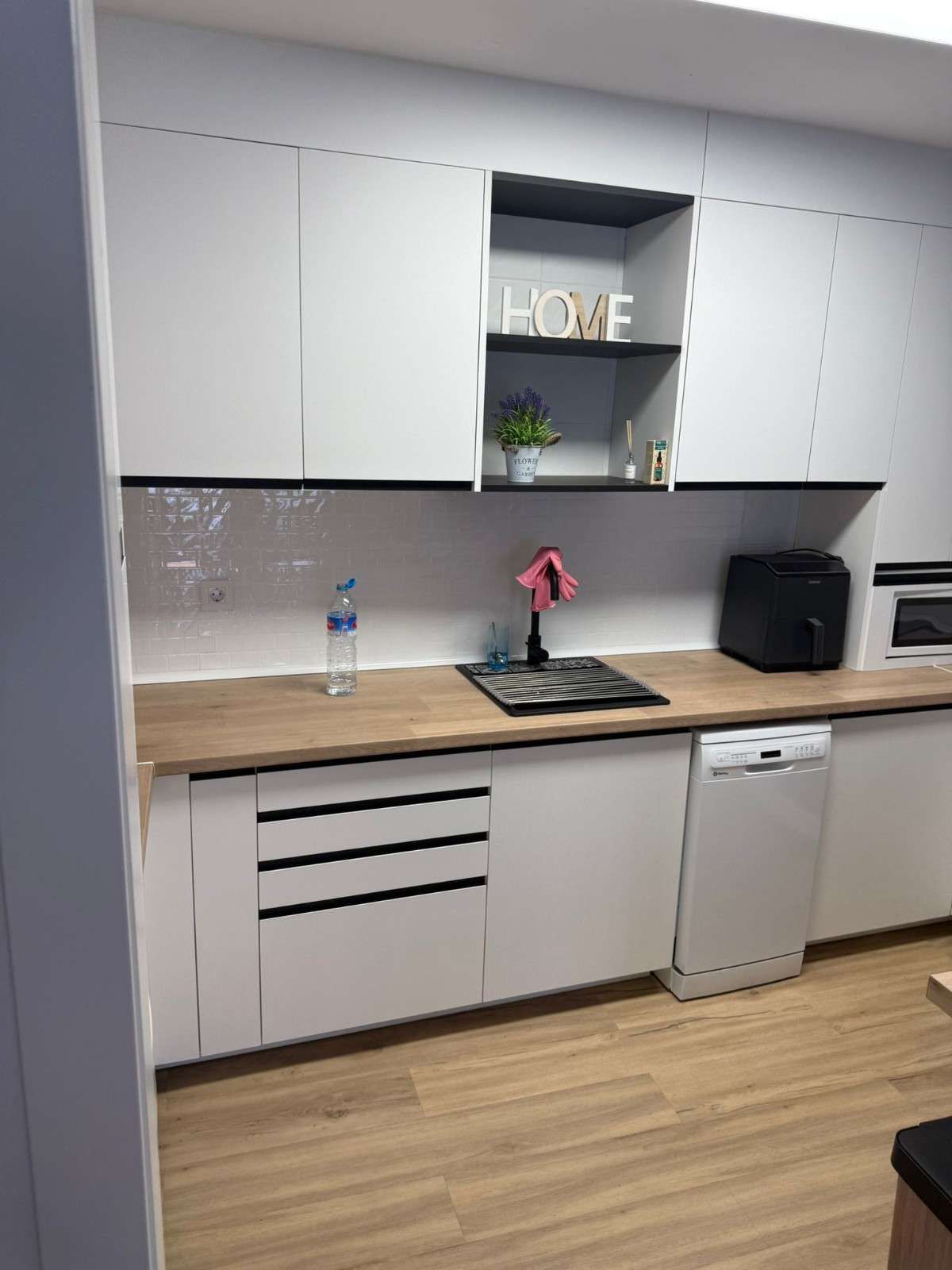 Cocina moderna blanca con encimera de madera, fregadero, armarios, microondas y lavavajillas.