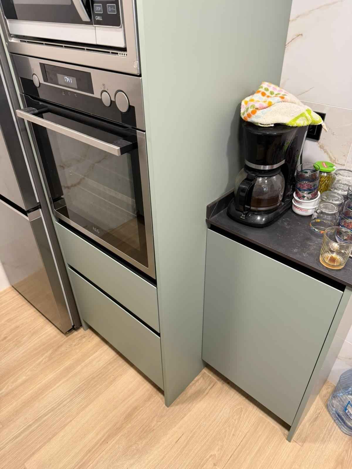 Rincón de cocina con horno empotrado, cafetera y tazas sobre una encimera junto a un frigorífico.