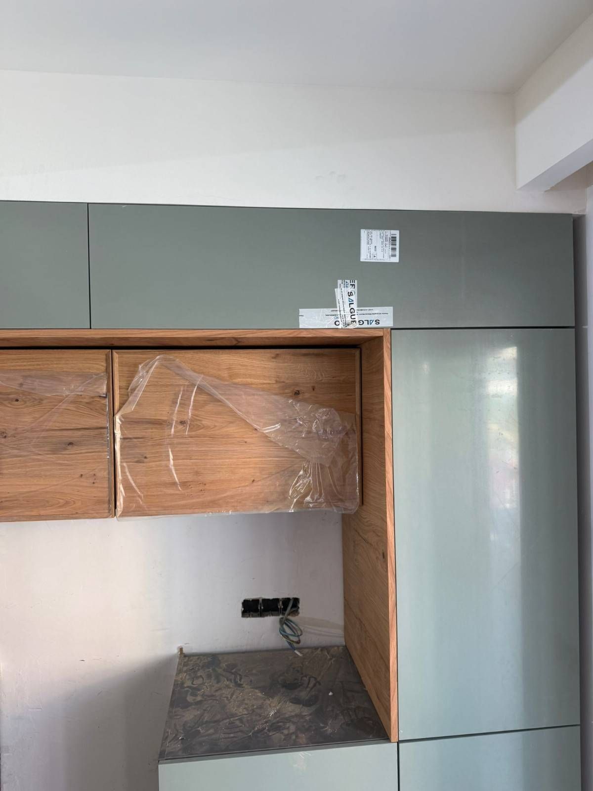 Armarios de cocina parcialmente instalados con acabado gris y de madera sobre una zona de encimera.