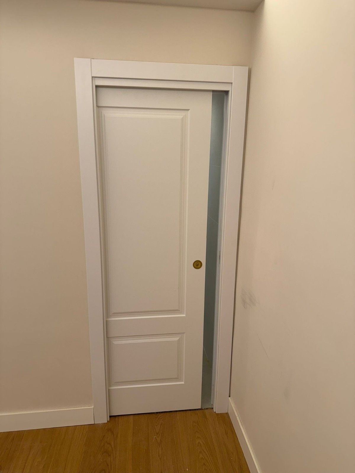 Puerta interior blanca en una habitación beige con suelo de madera, ligeramente entreabierta.