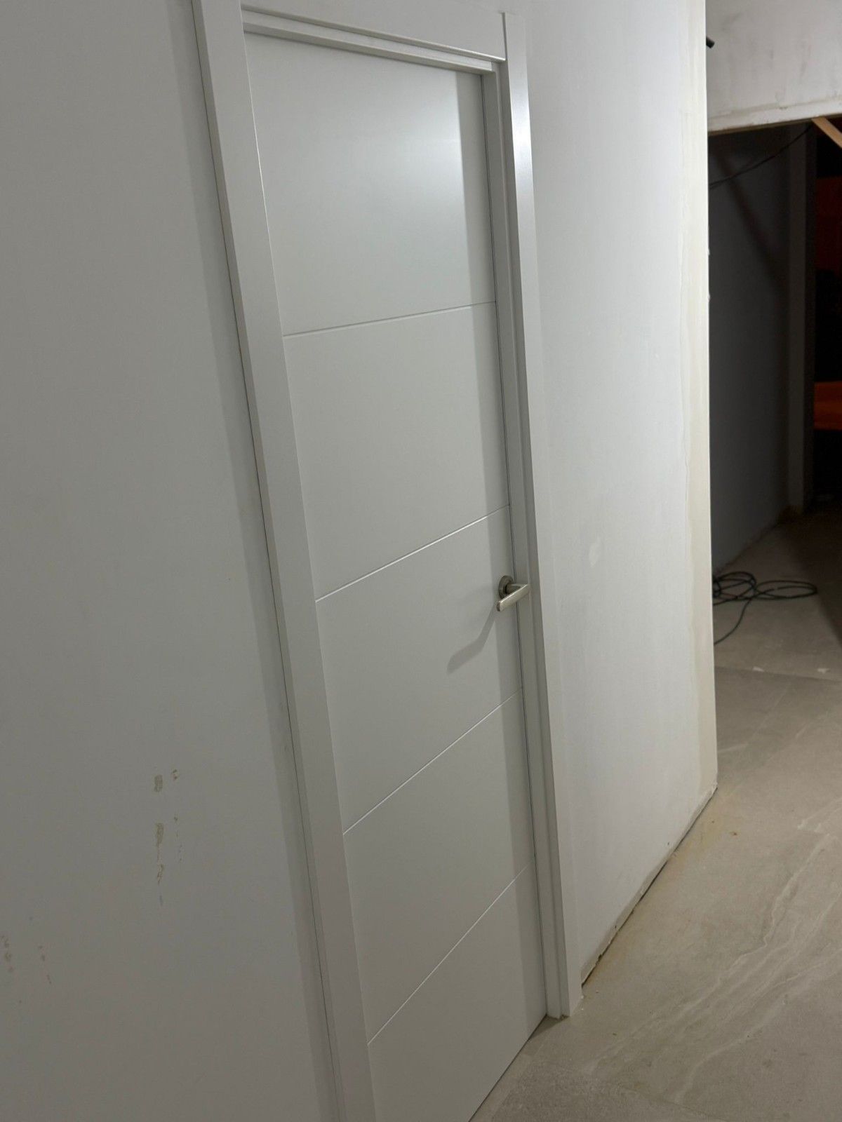 Pasillo interior blanco con una puerta blanca cerrada y paredes alicatadas, visto desde un ángulo.