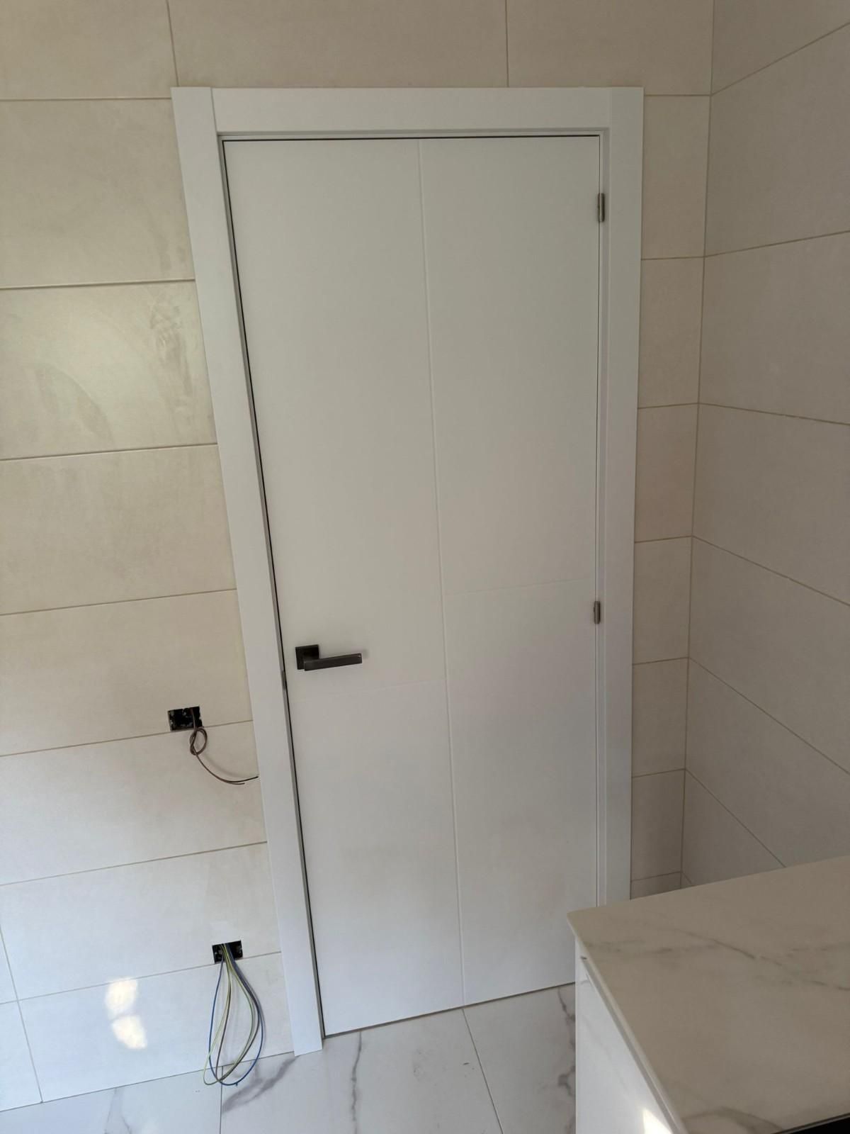 Puerta interior blanca en una habitación alicatada con tirador negro y toma de corriente en la pared cercana.
