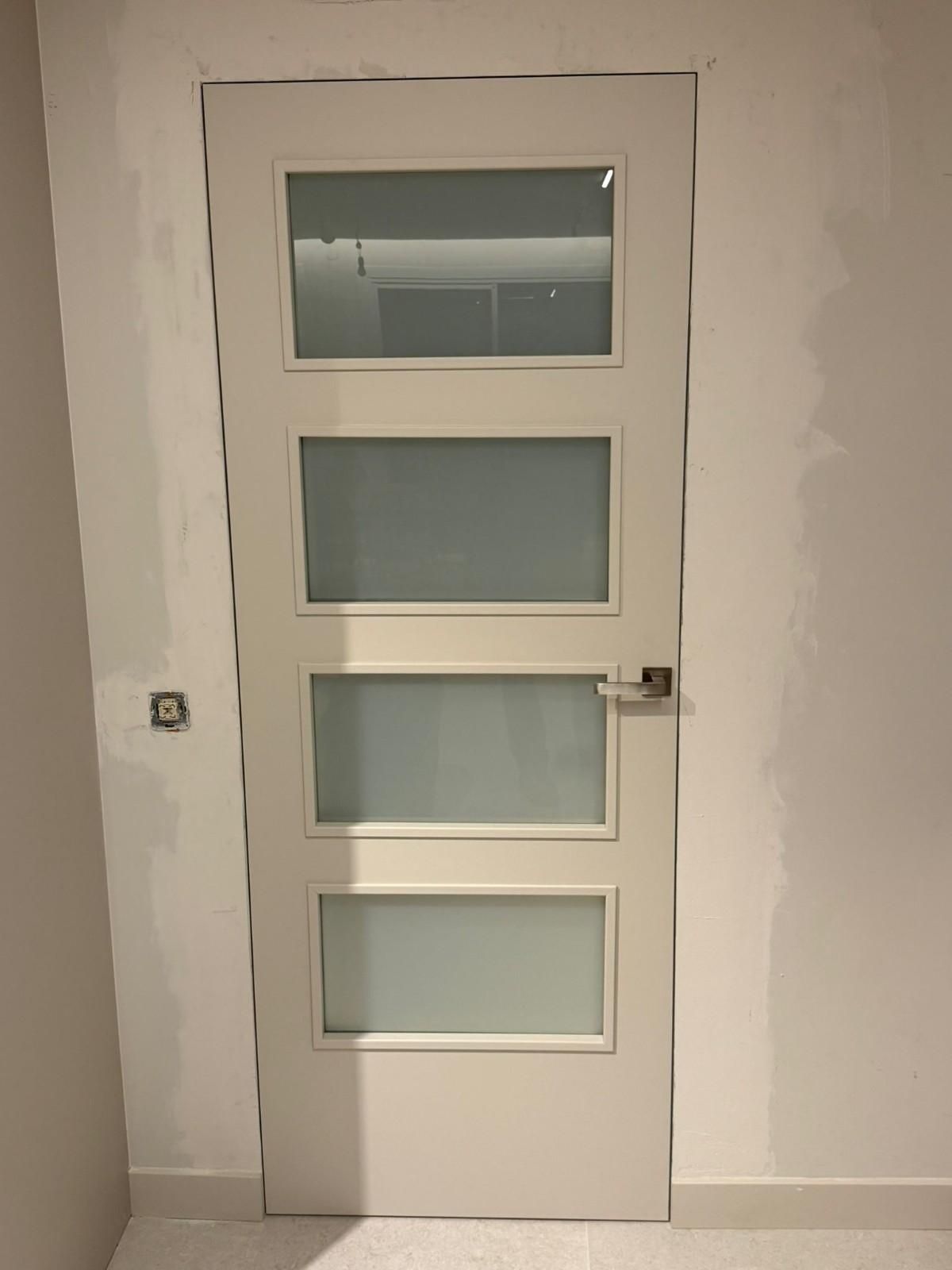 Puerta interior blanca con cuatro paneles de vidrio esmerilado en una pared lisa.