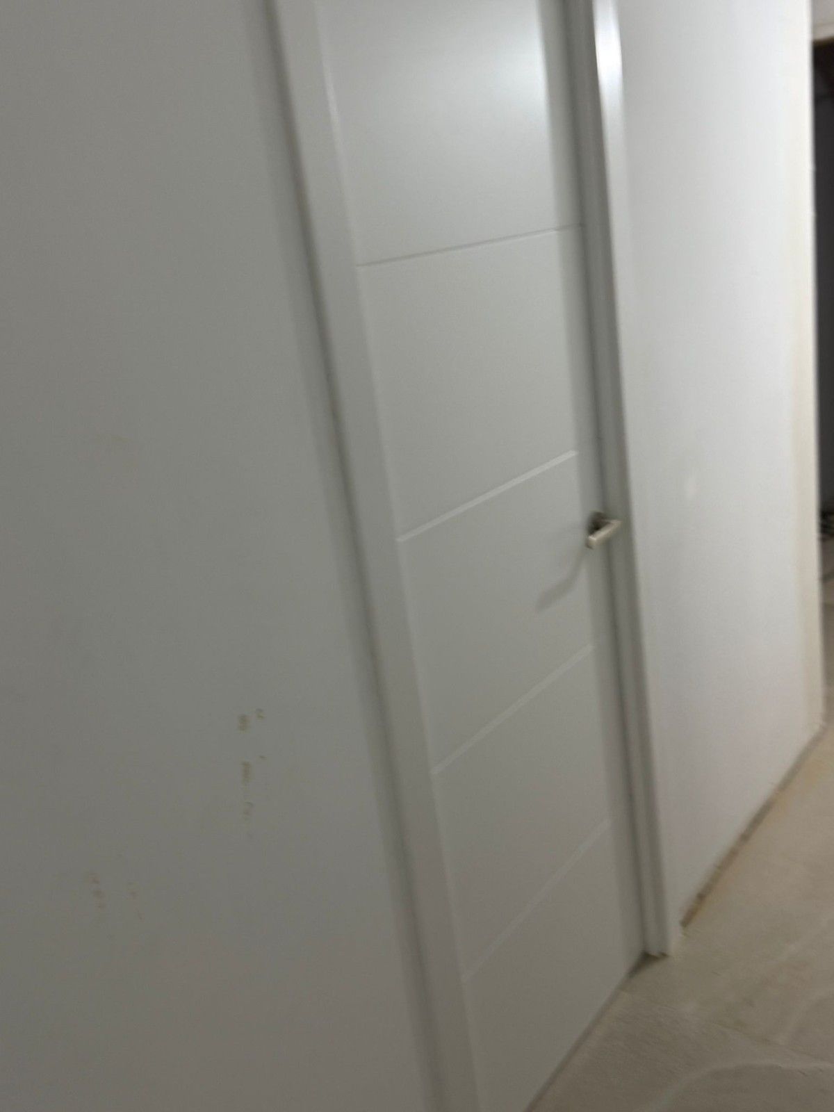 Pasillo interior blanco con puerta cerrada y baldosas beige en el suelo.