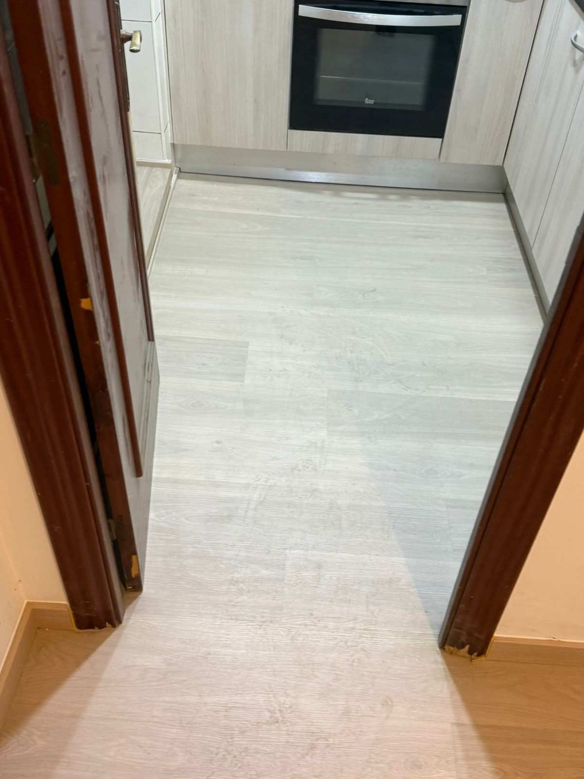 Entrada de cocina estrecha con suelo de madera clara que da a armarios blancos y un horno.