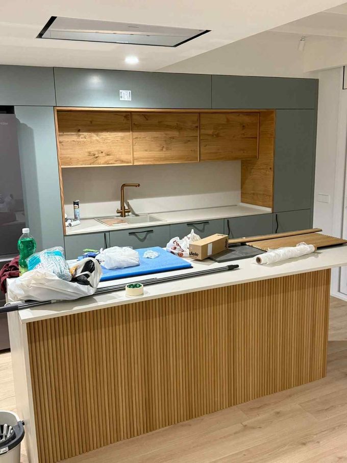 Cocina moderna vacía en proceso de renovación con isla de madera sin acabado y estanterías abiertas.
