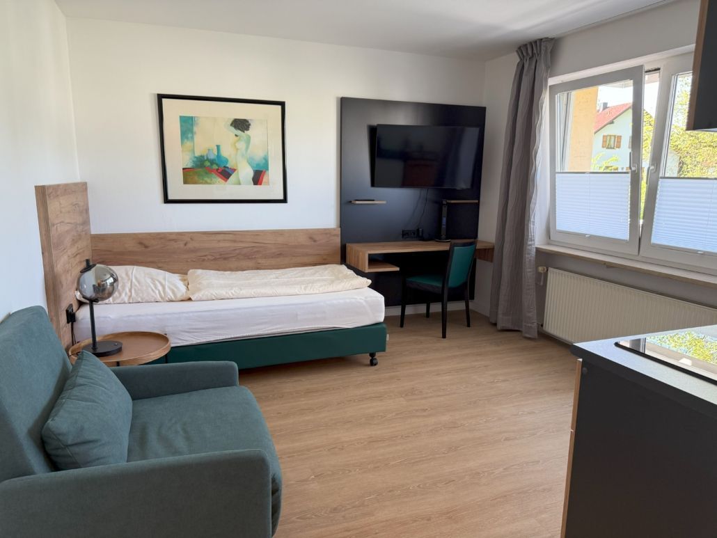 Studio-Apartment mit Bett, Schreibtisch, Sofa und Fenster.