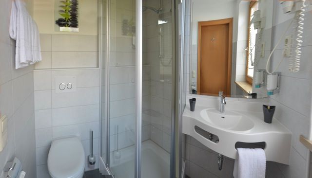 Kleines Badezimmer mit Toilette, Dusche, Waschbecken und Handtüchern. Helle, geflieste Wände.