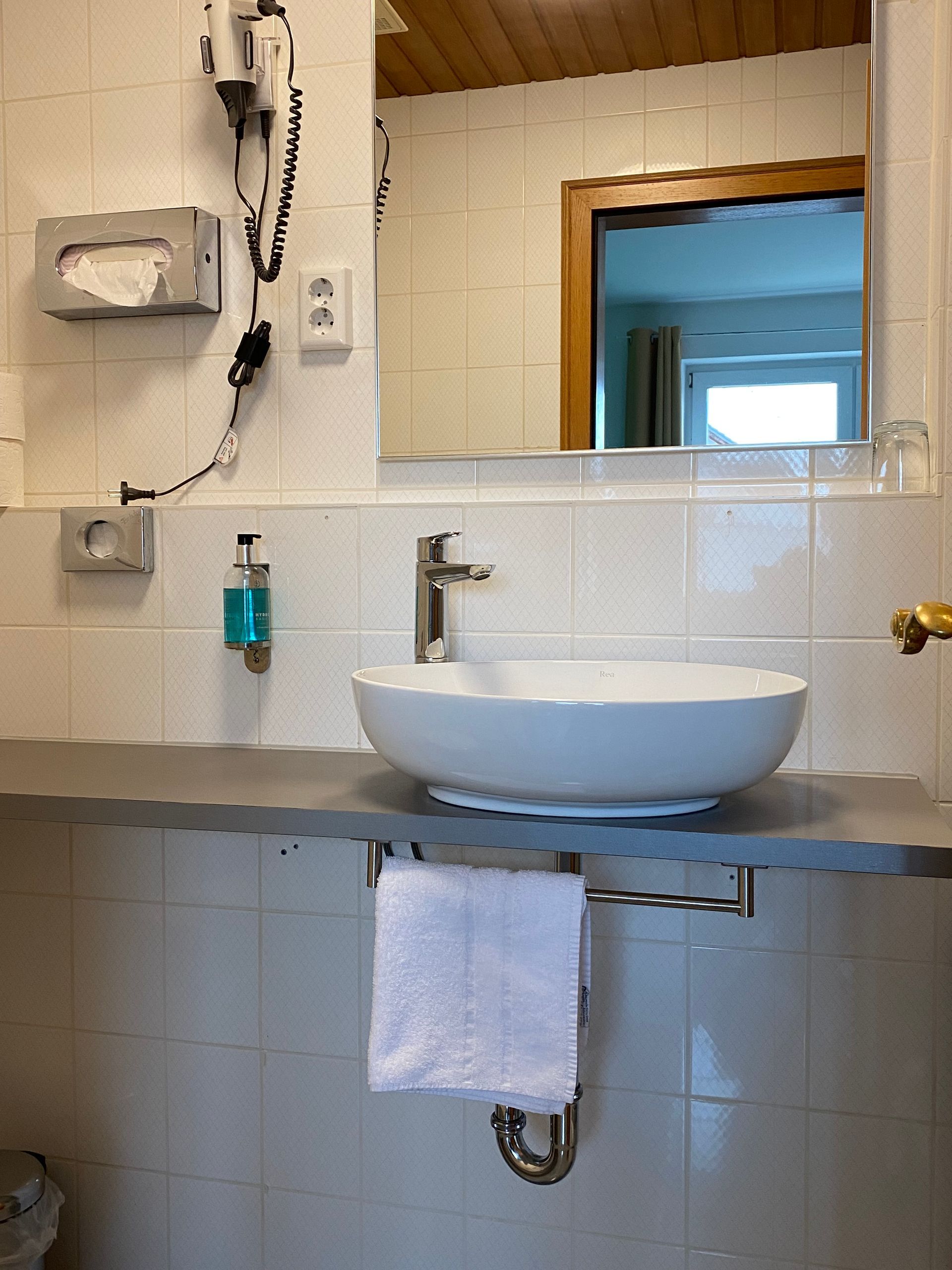 Badezimmerwaschbecken mit rundem, weißem Becken, verchromter Armatur, Handtuchhalter und Spiegel.