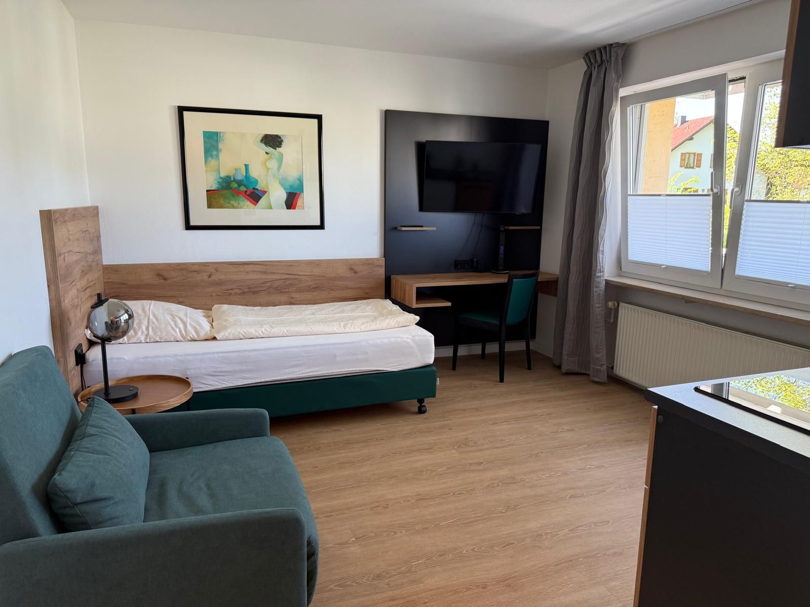 Hotelzimmer mit Bett, Schreibtisch, rotem Stuhl, Fenster und Fernseher.