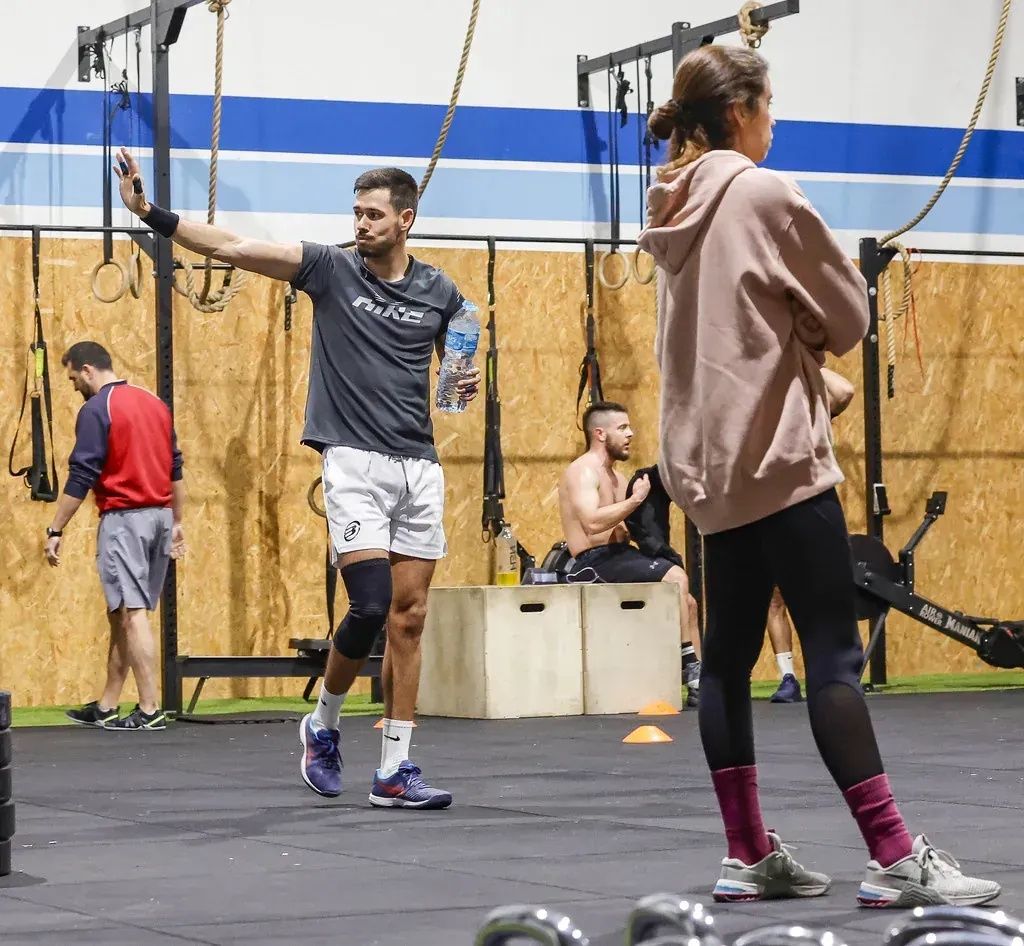 Escena de gimnasio: Hombre con el brazo levantado sosteniendo una botella de