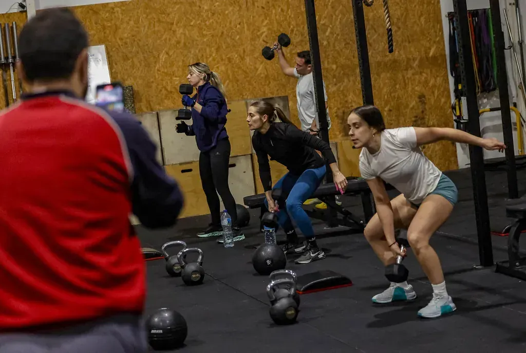 Gente haciendo pesas en un gimnasio. Una persona con camisa roja filma.