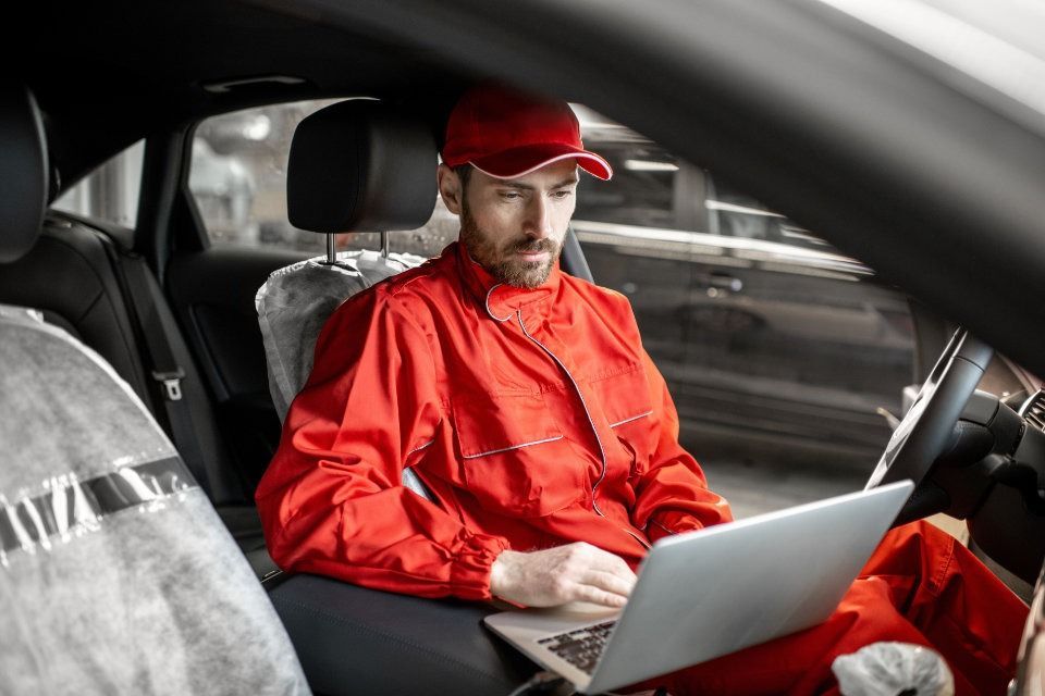 Un hombre está sentado en el asiento trasero de un automóvil utilizando una computadora portátil.