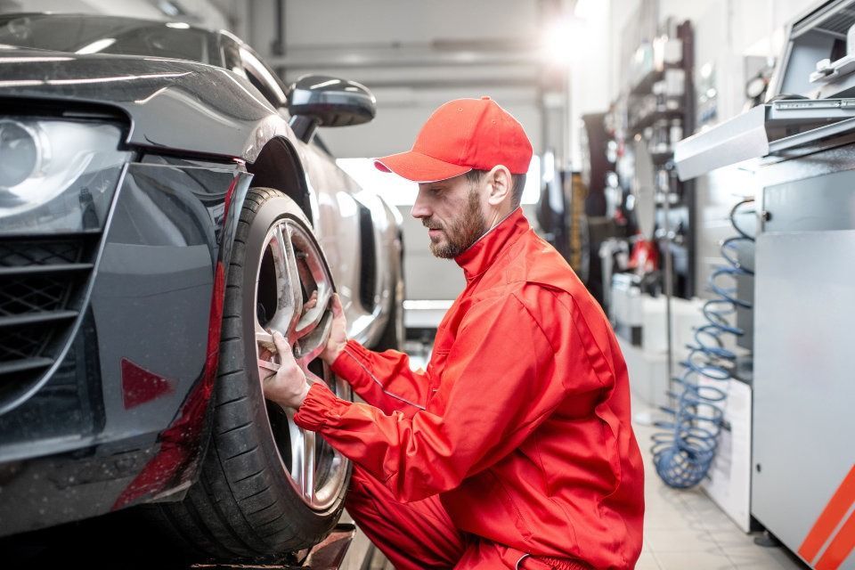 Un hombre con uniforme rojo está trabajando en una rueda de coche en un garaje.