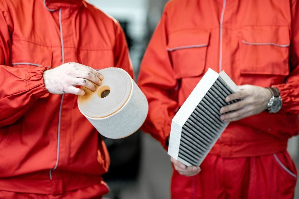 Dos hombres con uniformes rojos sostienen filtros de aire en sus manos.