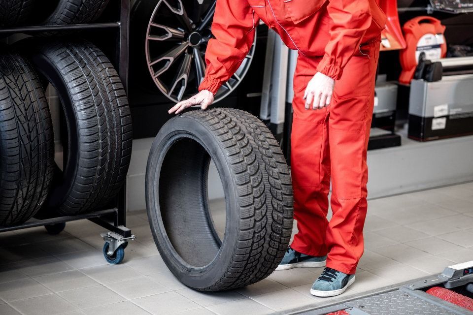 Un hombre con un traje rojo sostiene un neumático en un garaje.