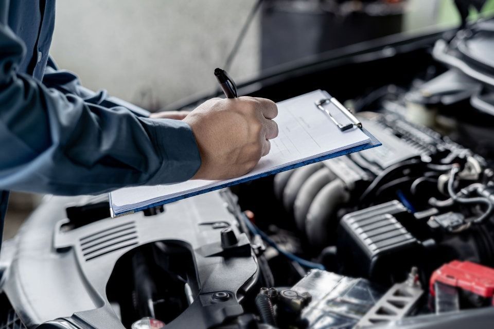 Un mecánico está escribiendo en un portapapeles mientras trabaja en un automóvil.