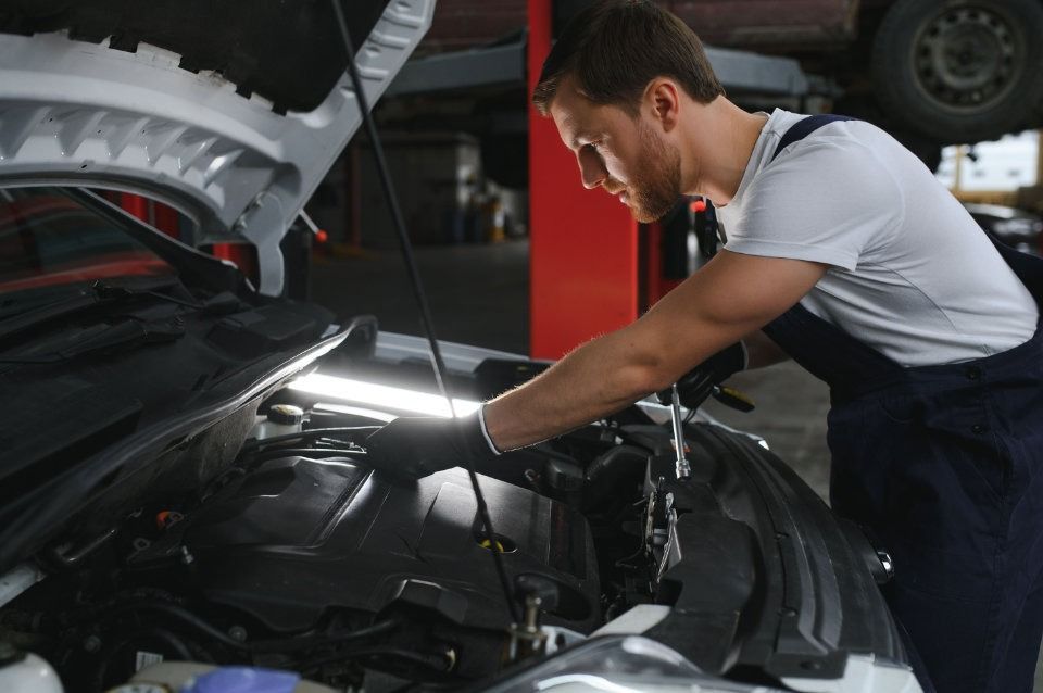 Un hombre está trabajando en el motor de un coche en un garaje.