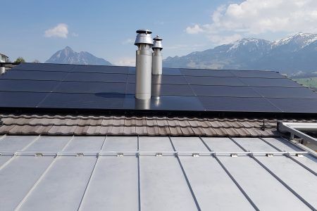 Ein Dach mit Sonnenkollektoren und Schornsteinen darauf mit Bergen im Hintergrund, Sepp Wagner GmbH