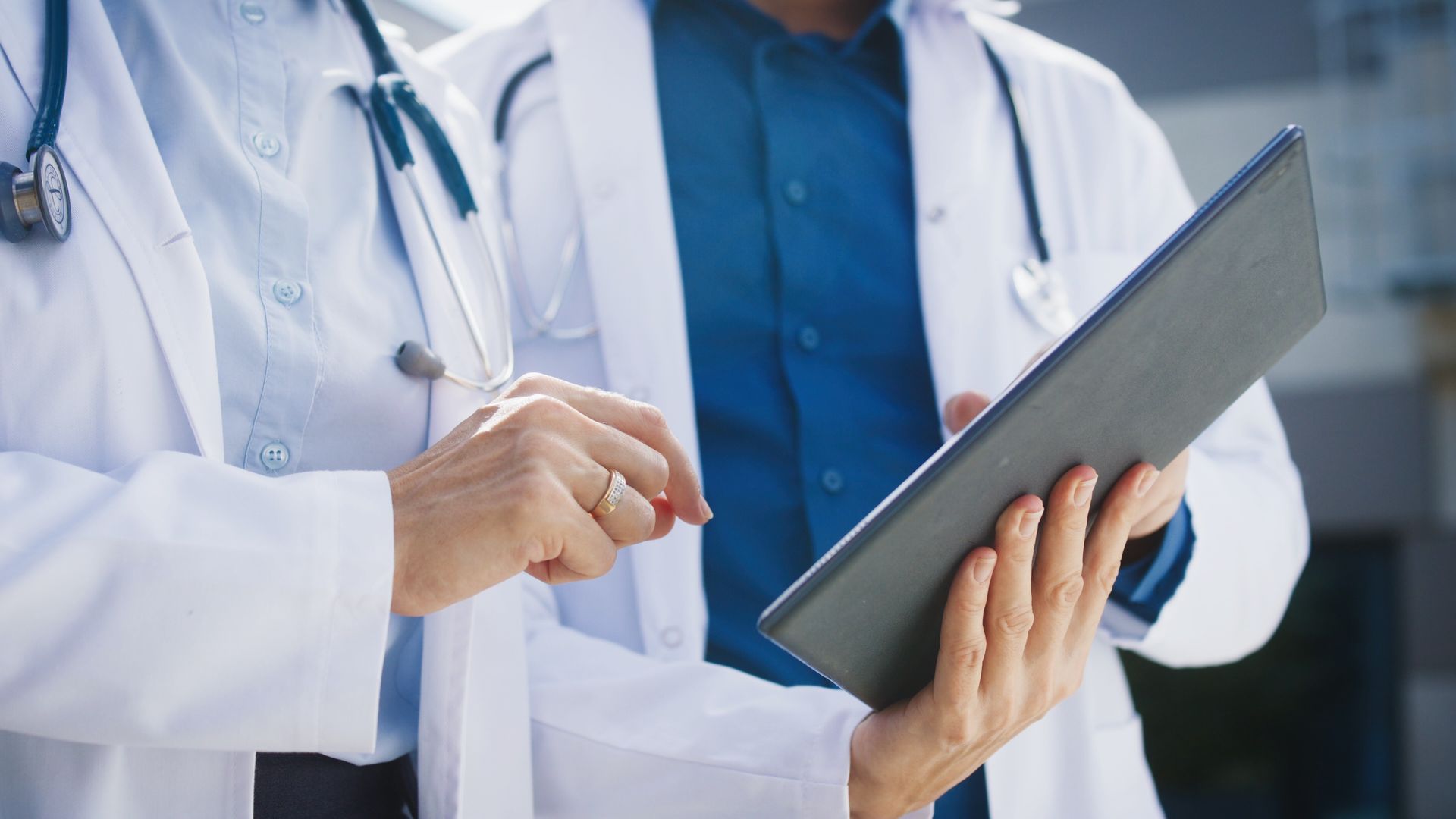 Medici in camice bianco esaminano le informazioni di un paziente su un tablet in un ambiente ospedaliero.