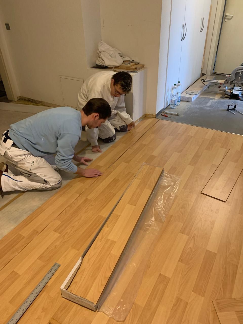 Zwei Männer arbeiten in einem Raum an einem Holzboden.