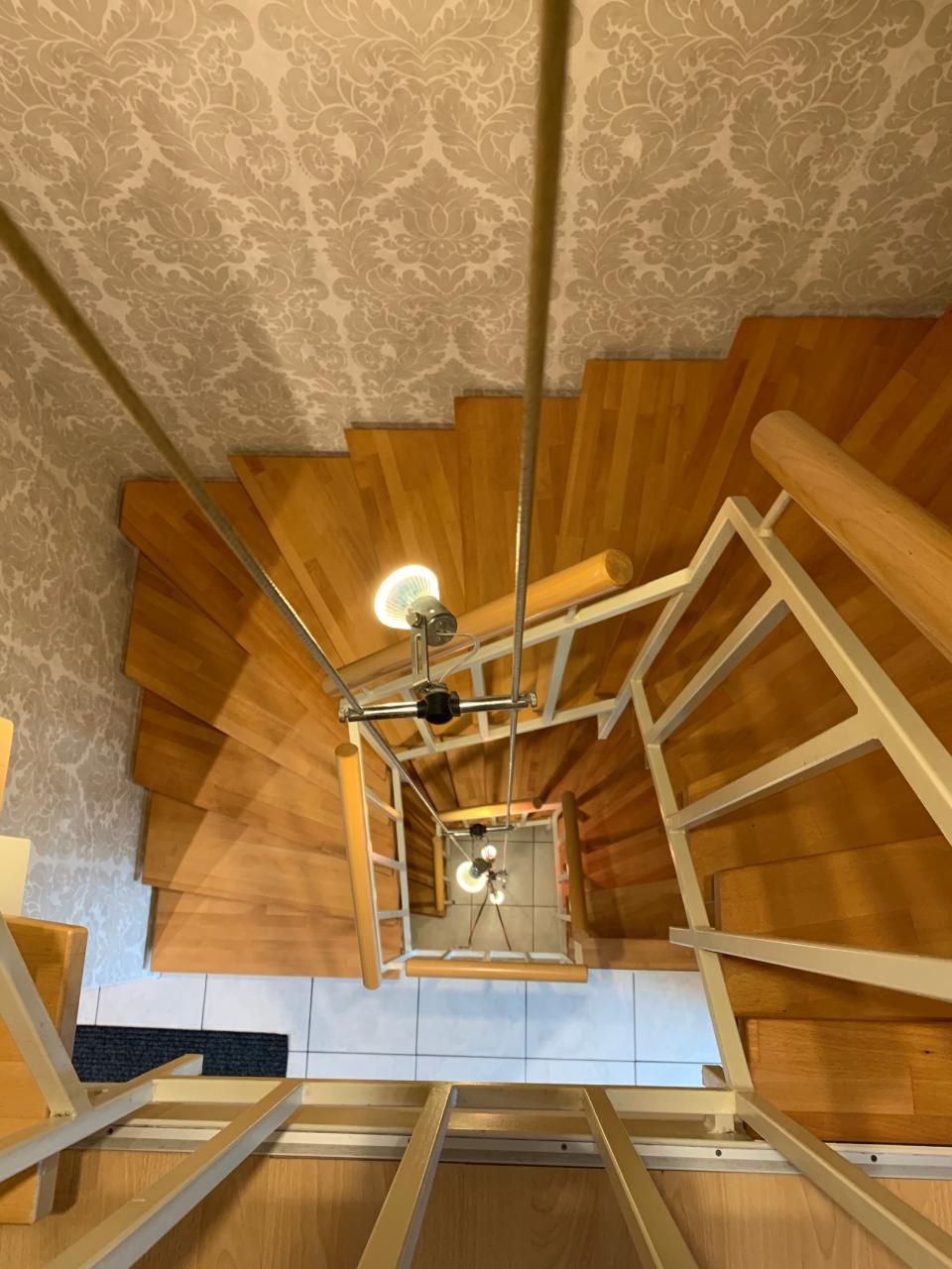 Blick nach unten auf eine hölzerne Wendeltreppe mit Metallgeländer.