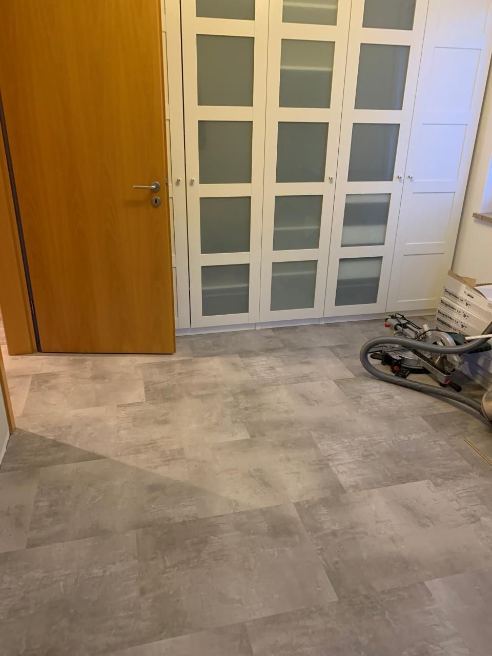 Ein Raum mit einer Holztür und einem grauen Fliesenboden.