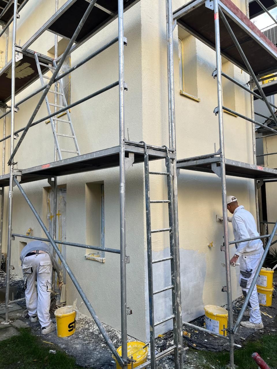 Zwei Männer streichen die Seite eines Gebäudes.