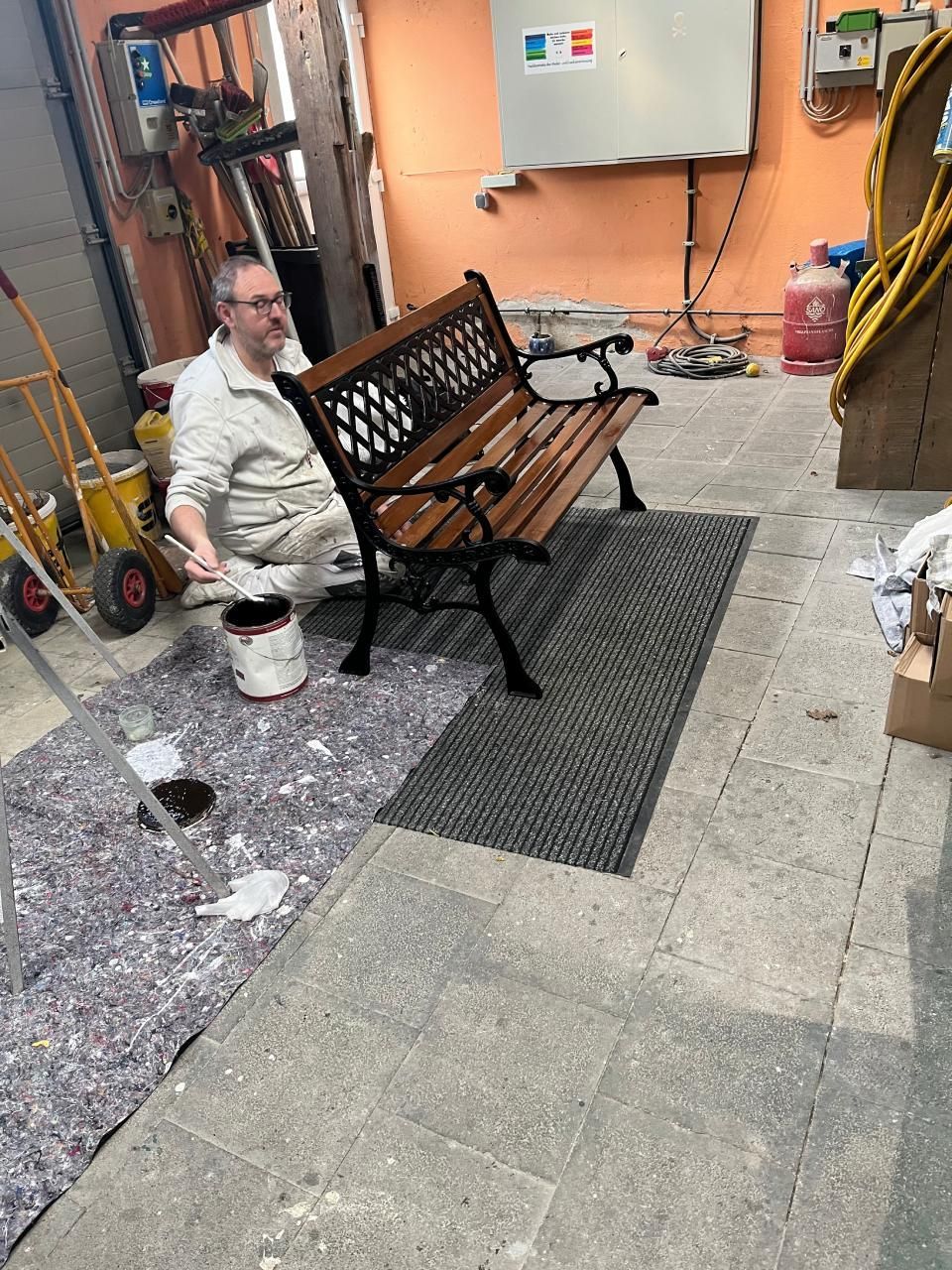 Ein Mann sitzt auf dem Boden und streicht eine Holzbank.