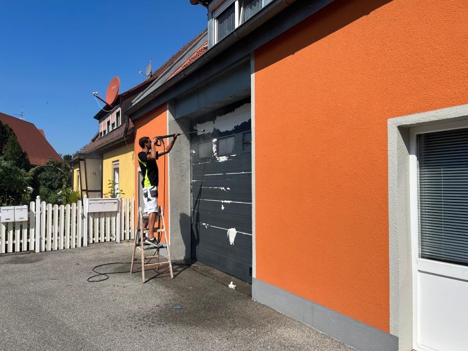 Ein Mann steht auf einer Leiter und streicht die Seite eines Gebäudes.