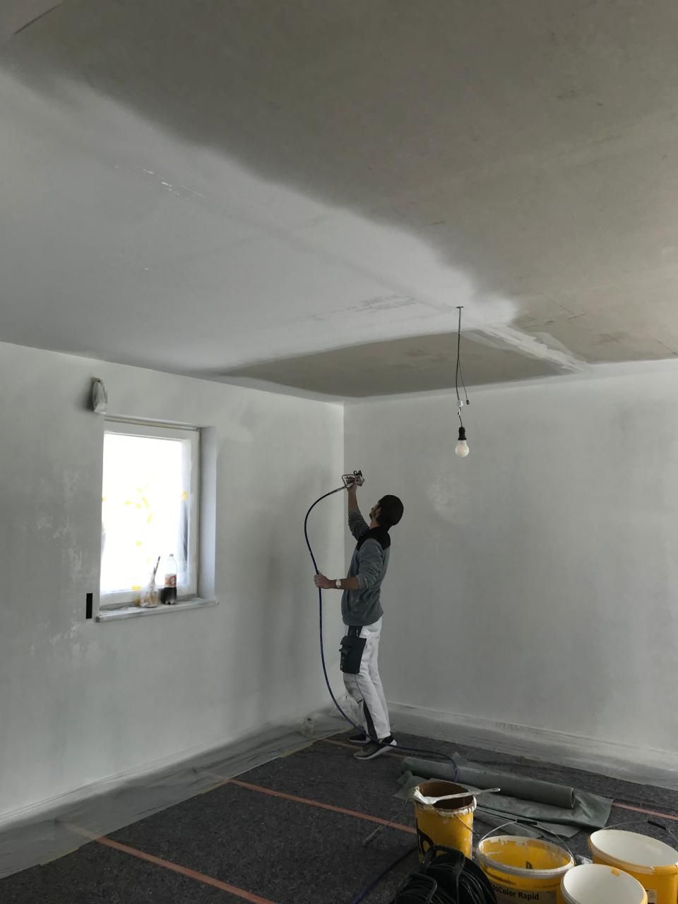 Ein Mann streicht mit einer Spritzpistole die Decke eines Raumes.