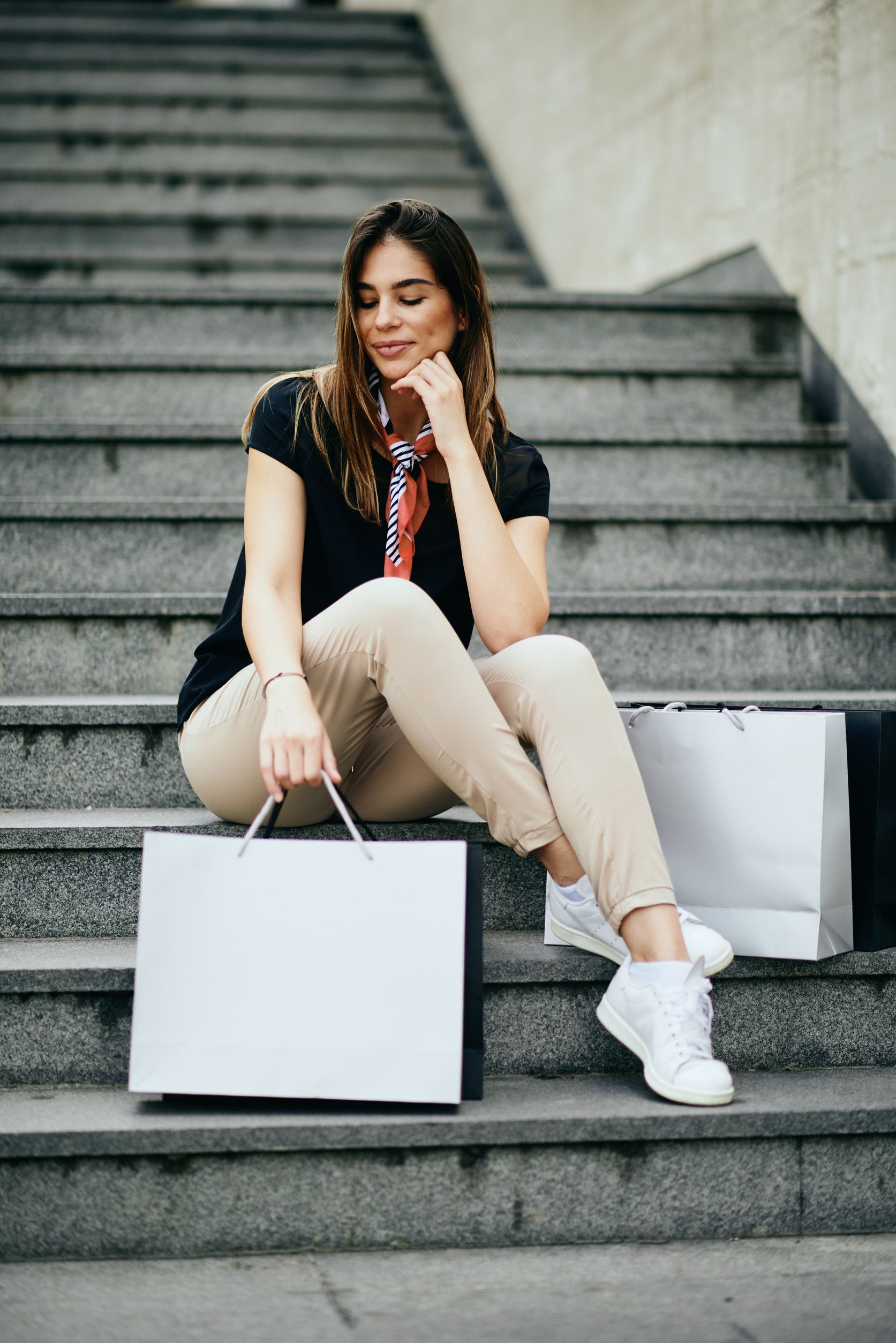 Una mujer está sentada en las escaleras con bolsas de compras.