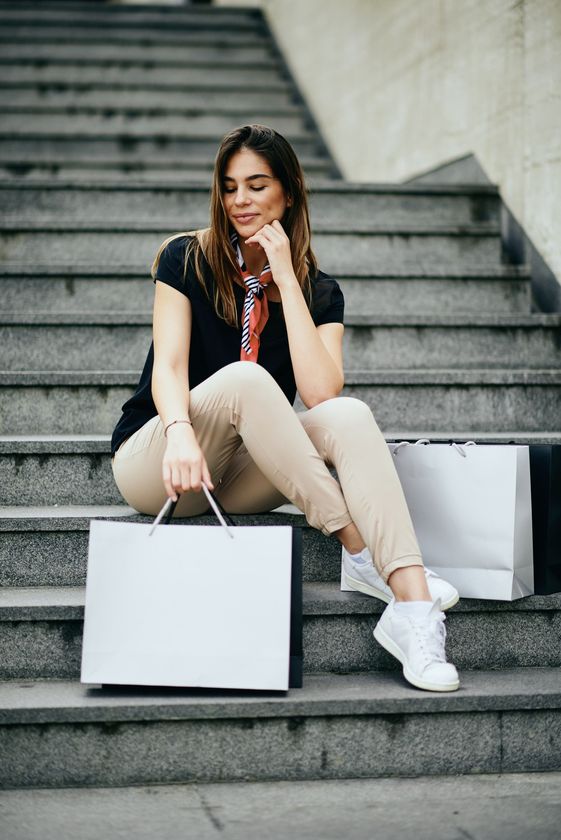 Una mujer está sentada en las escaleras con bolsas de compras.
