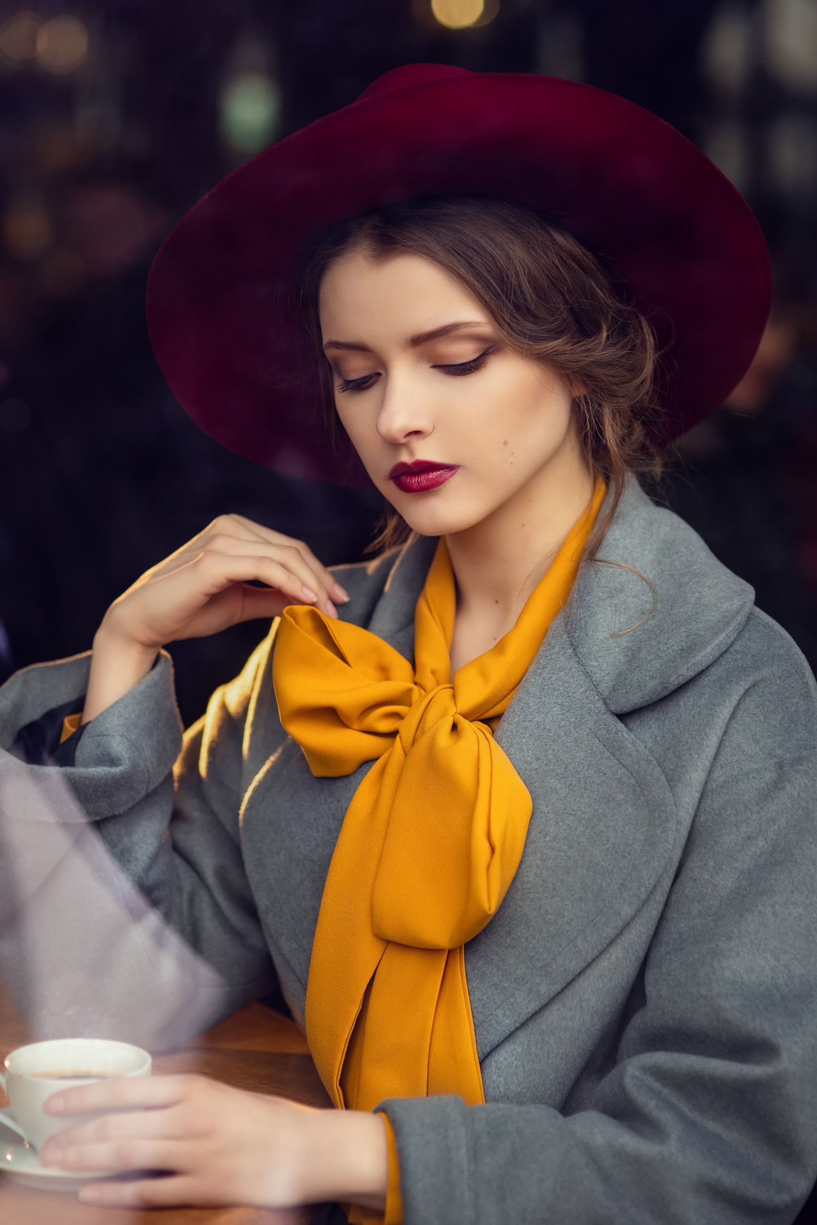 Una mujer con sombrero y bufanda está sentada en una mesa con una taza de café.