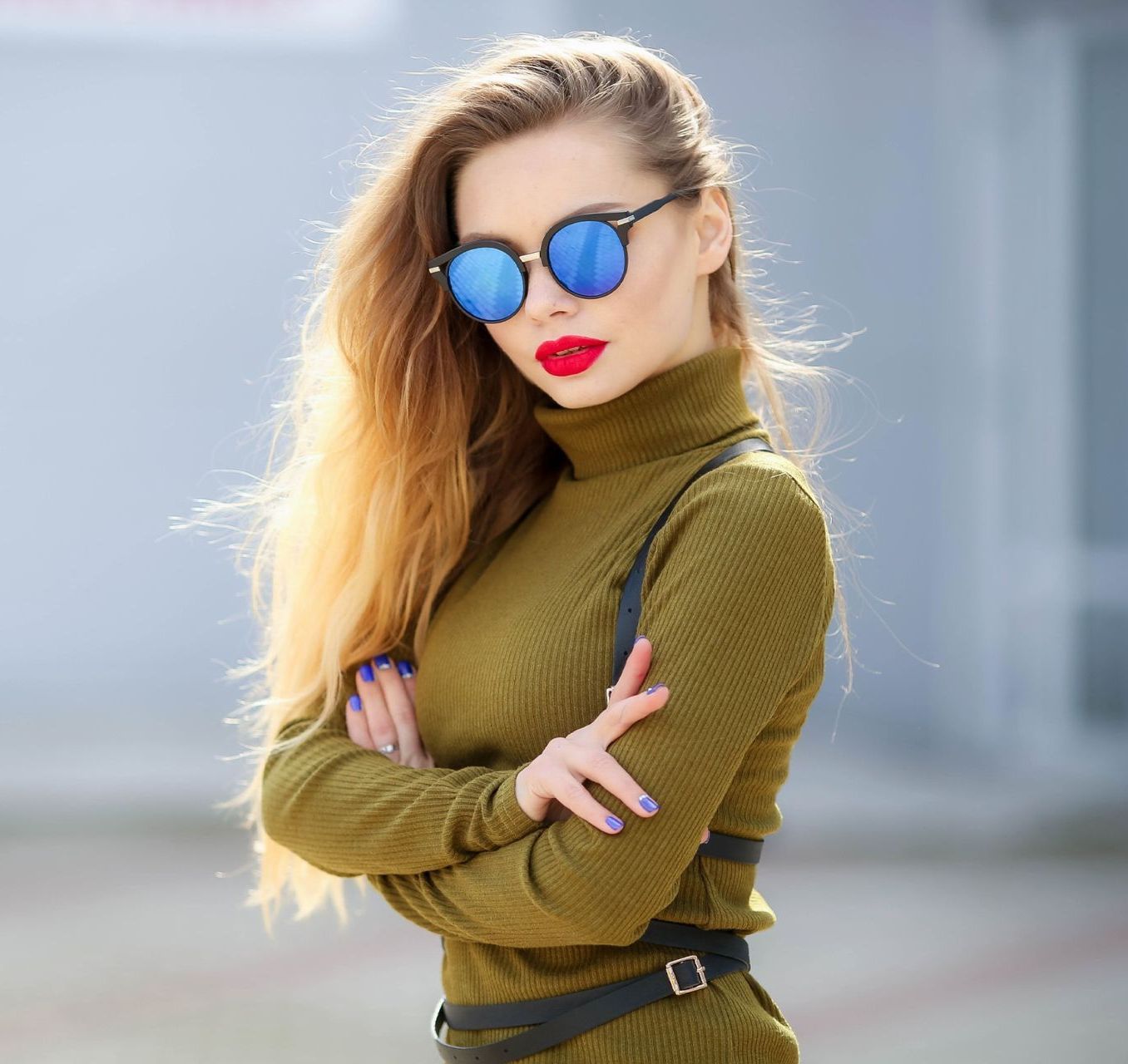 Una mujer que lleva un jersey de cuello alto verde y gafas de sol está de pie con los brazos cruzados.