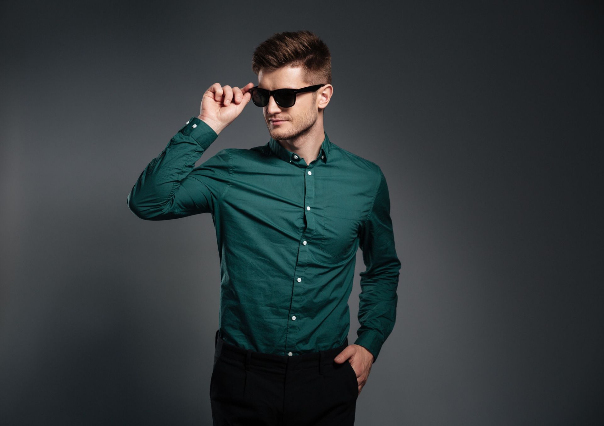 Un hombre con una camisa verde y pantalones negros lleva gafas de sol.