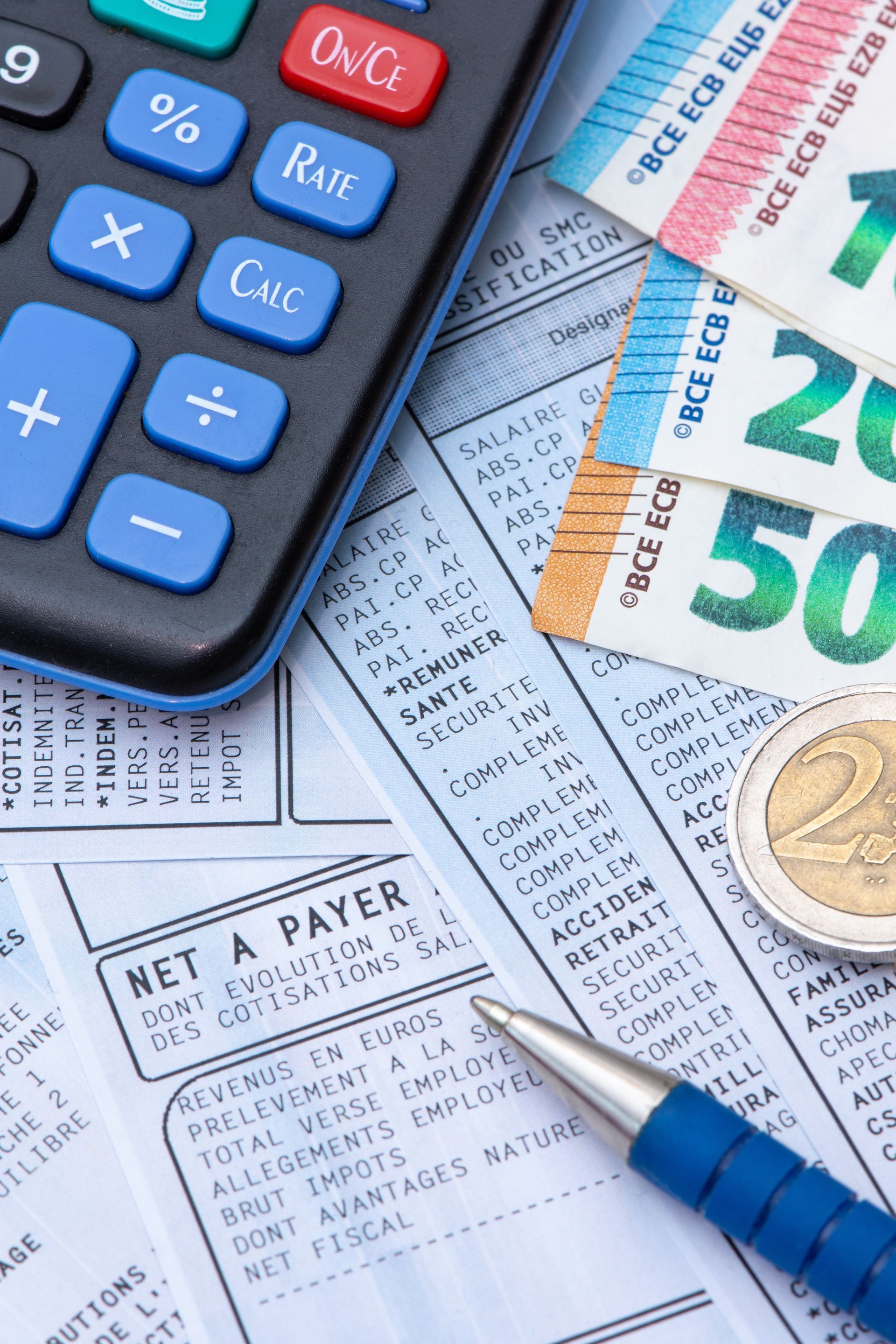 Calculatrice, billets de banque et pièces de monnaie sur un bulletin de paie, avec un stylo, illustrant des calculs financiers et un paiement