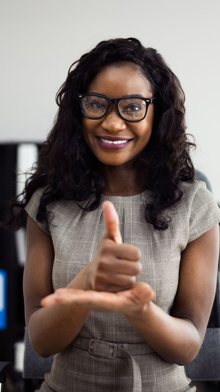 Une femme portant des lunettes, sourit et parle en langage des signes