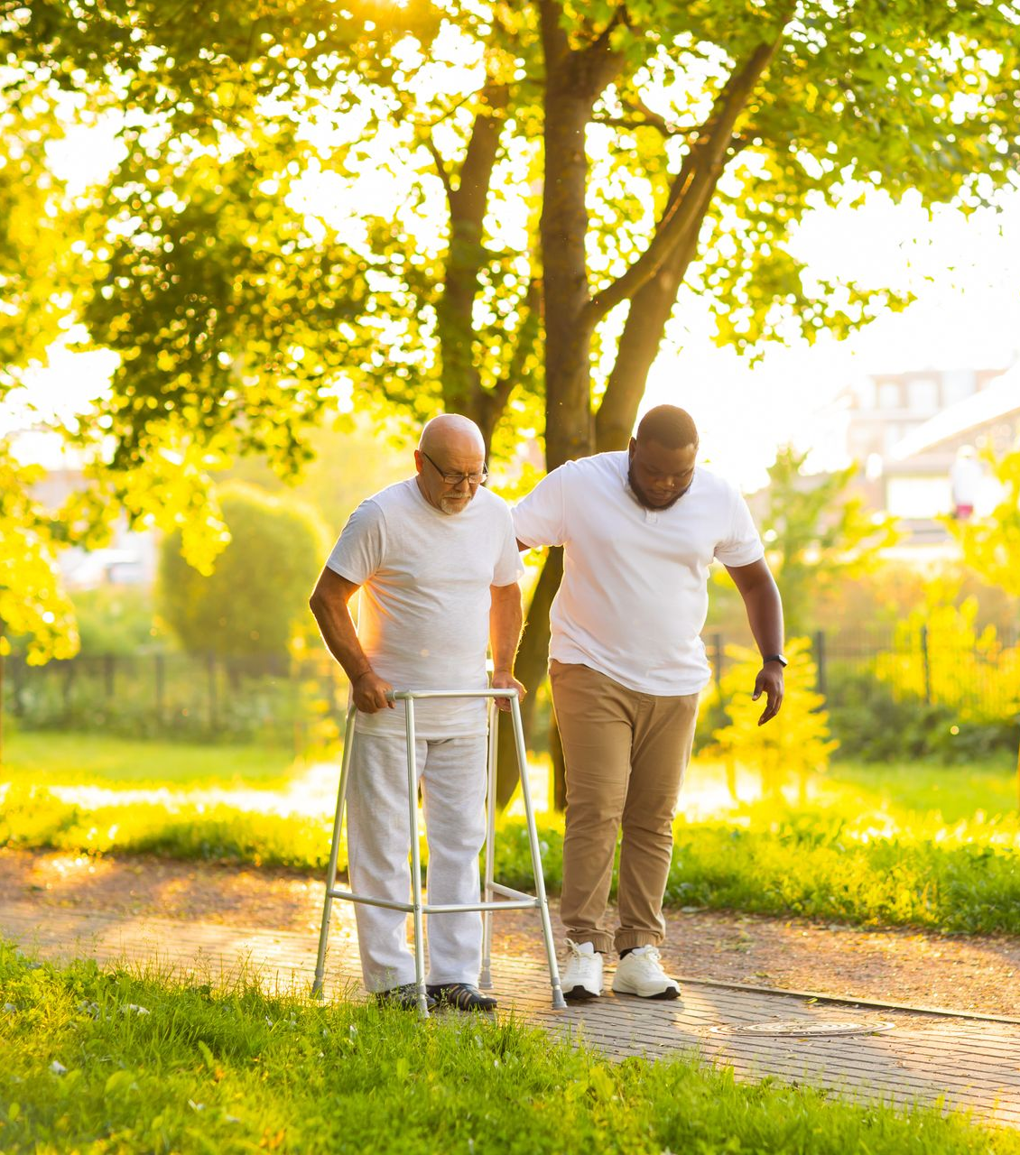 Un homme utilisant un déambulateur est assisté par un autre homme sur un chemin ensoleillé