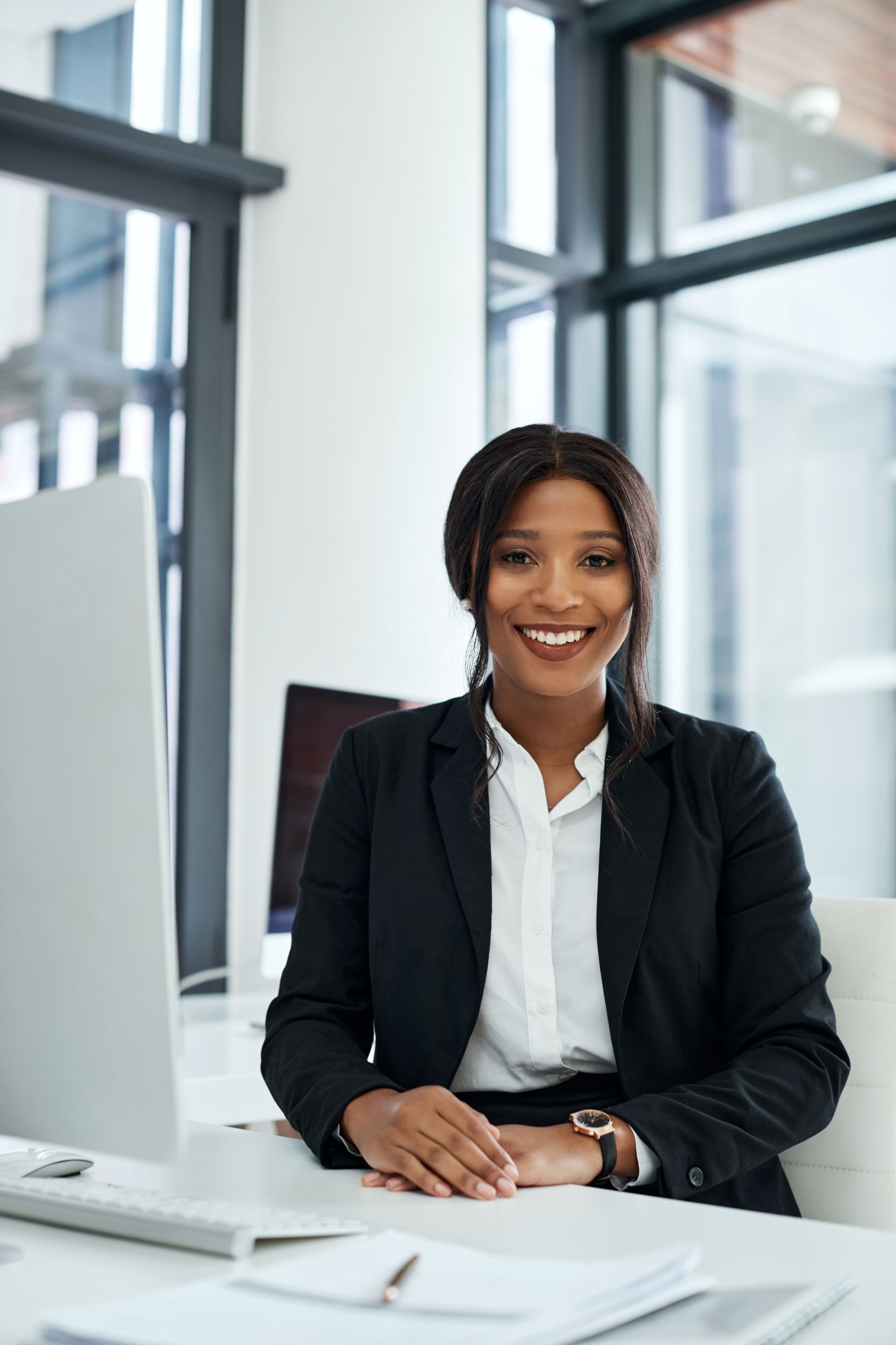 Femme en blazer noir, souriante, à un bureau